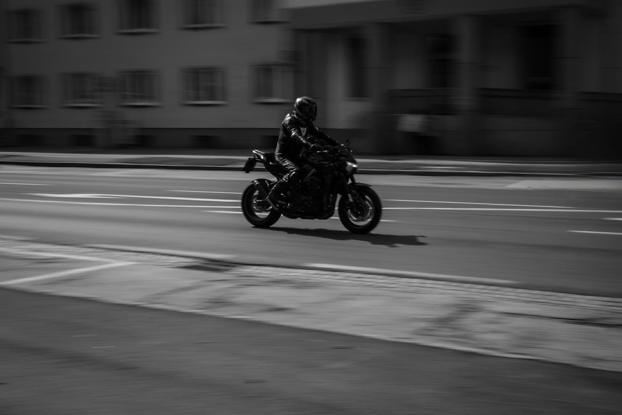 Motorcyclist riding through city streets in black and white, highlighting speed and motion.