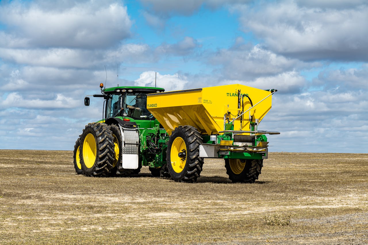 Modern tractor with trailer sowing grain on agricultural field in countryside against cloudy blue sky